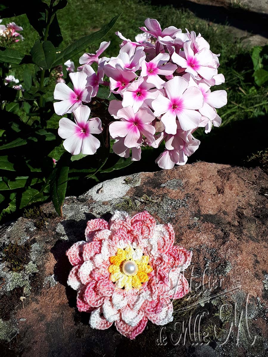 Une barrette en forme de fleur rose et blanche, avec 3 rangées de pétales et son cœur jaune à perle nacrée. Composition : Fil cablé 100% coton égyptien. Support de barrette en métal. Perle. Fleur réalisée et adaptée d'après le tuto vidéo de NotikaLand crochet and knitting : https://youtu.be/YA7xpcC7ueo