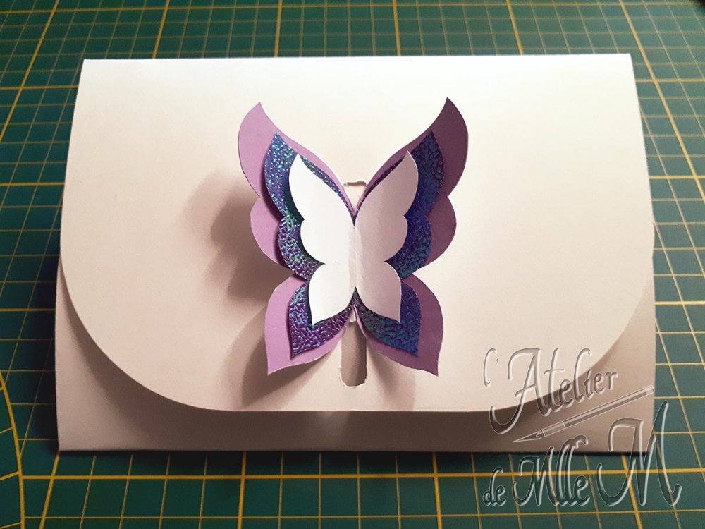 Une enveloppe en papier cartonné avec une fermeture 3D en forme de papillon. Composition : Papier de différentes couleurs et différents grammages.