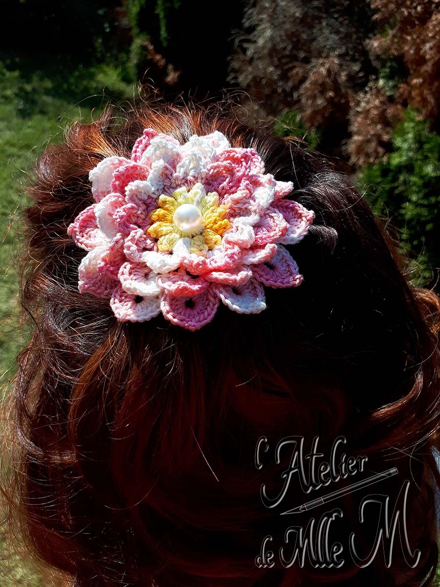 Une barrette en forme de fleur rose et blanche, avec 3 rangées de pétales et son cœur jaune à perle nacrée. Composition : Fil cablé 100% coton égyptien. Support de barrette en métal. Perle. Fleur réalisée et adaptée d'après le tuto vidéo de NotikaLand crochet and knitting : https://youtu.be/YA7xpcC7ueo