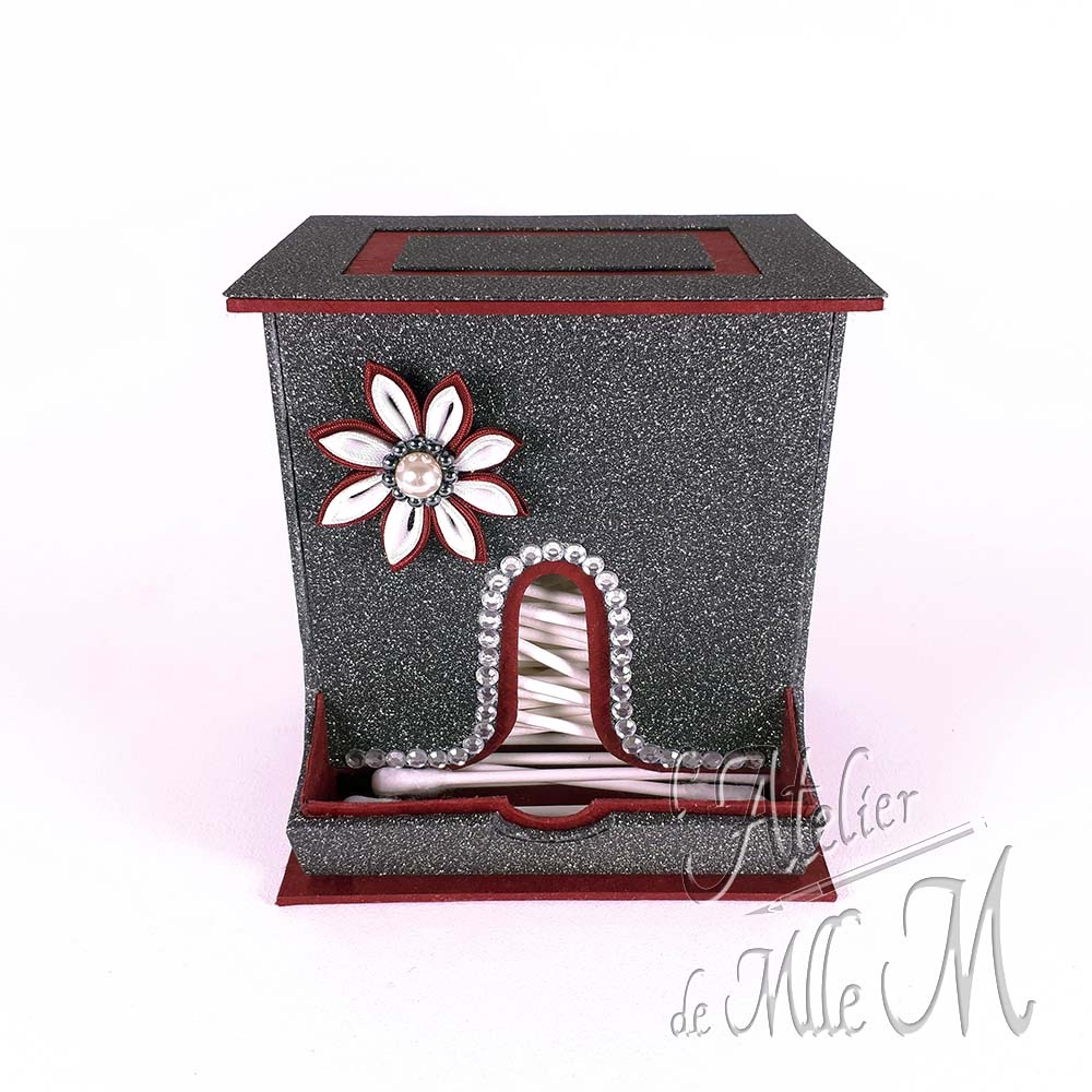 Un distributeur de cotons de tige en carton fait sur mesure agrémenté de sa fleur tsumami en satin. Composition : Carton – Papier cadeau pailleté. Papier lokta – Strass. Satin – Perles. Dimensions : x (H) x x (P) x x (l) cm.