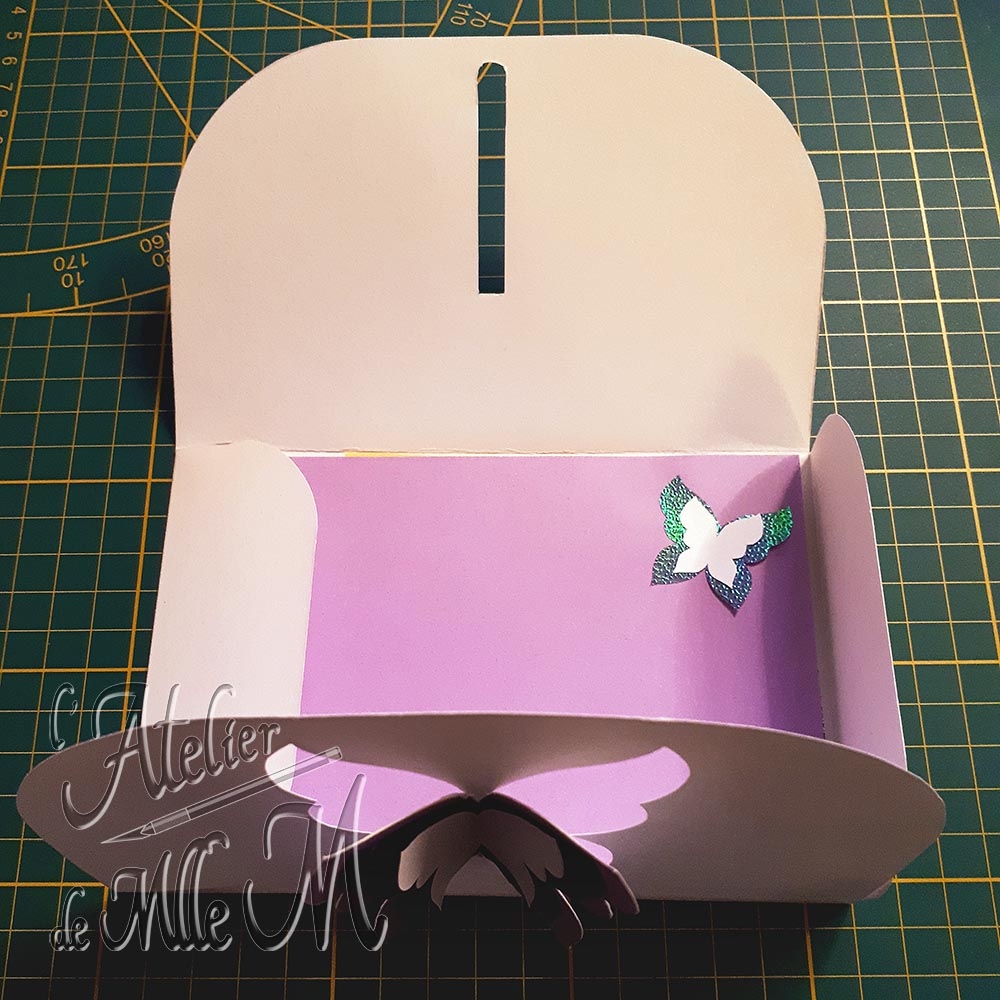 Une enveloppe en papier cartonné avec une fermeture 3D en forme de papillon. Elle contient un message avec un petit rappel de la thématique papillon. Composition : Papier de différentes couleurs et différents grammages.