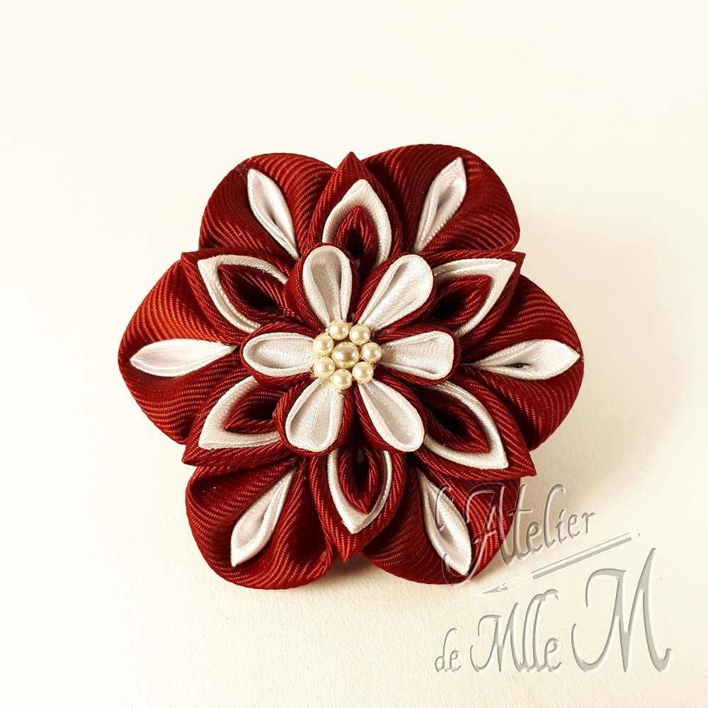 Une fleur bordeaux & blanche réalisée selon l'art tsumami zaiku. Composition : Rubans de satin - Perles nacrées. Une revue complète à lire pour rétablir la vérité sur les Tsumami zaiku et les Kanzashi disponible sur https://www.latelierdemllem.com/verite-sur-tsumami-zaiku-kanzashi/