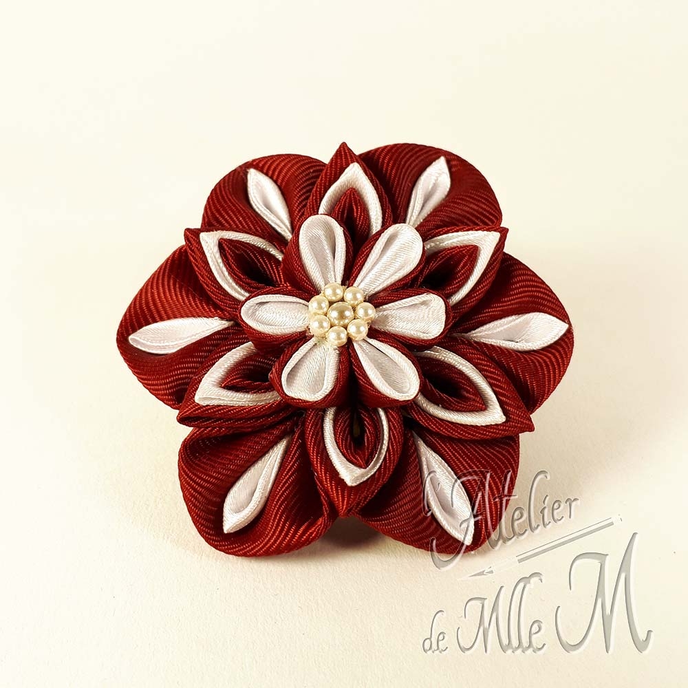 Une fleur bordeaux & blanche réalisée selon l'art tsumami zaiku. Composition : Rubans de satin - Perles nacrées. Une revue complète à lire pour rétablir la vérité sur les Tsumami zaiku et les Kanzashi disponible sur https://www.latelierdemllem.com/verite-sur-tsumami-zaiku-kanzashi/