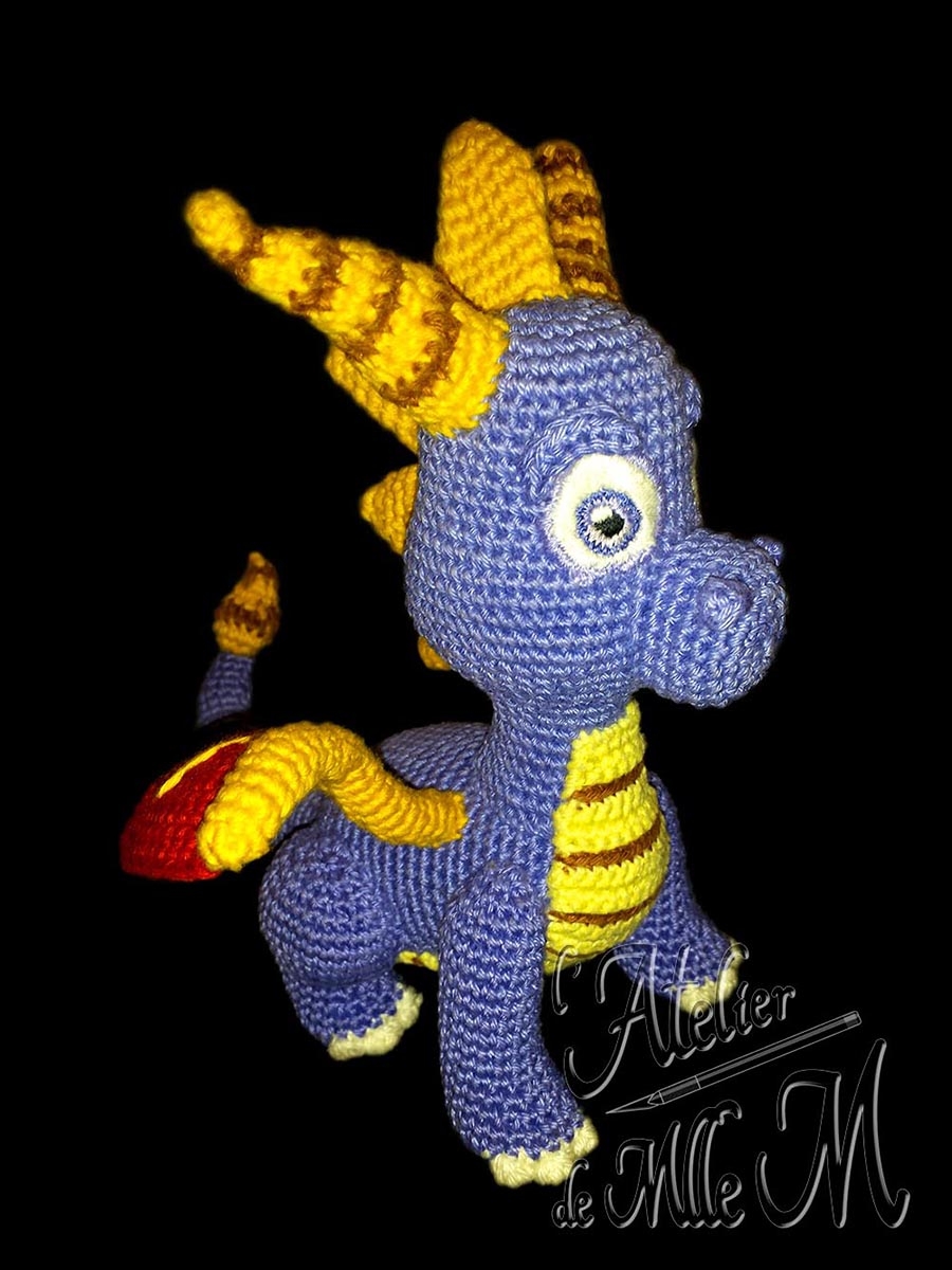 Dragon Spyro. Une représentation assez fidèle du dragon du célèbre jeu vidéo. Composition : Fil 100% coton et rembourrage polyester. Yeux brodés en coton mouliné. Dimensions : 19 x 15 x 18 cm.